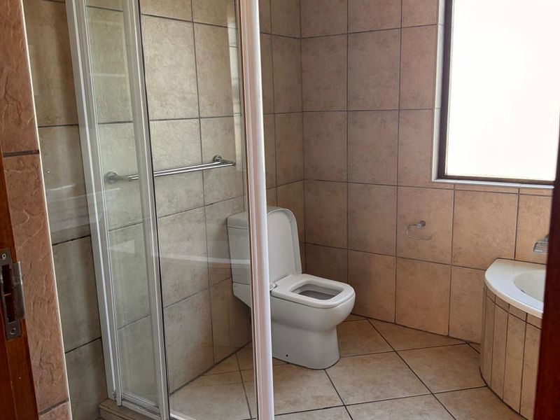 A functional bathroom featuring a shower enclosure, a built-in bathtub, and a toilet, finished with neutral floor-to-ceiling wall tiles.