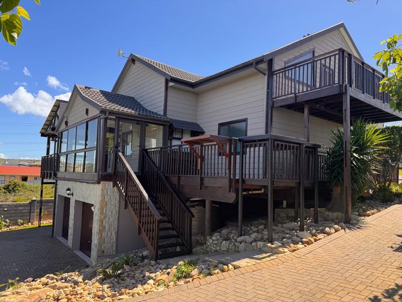 Rear view of a multi-level house featuring a large timber deck, balcony, stone-clad lower level, and paved driveway access to the garage.