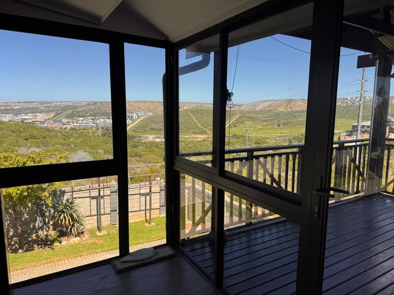An enclosed balcony featuring black aluminum frames, timber decking, and expansive views of the surrounding landscape.