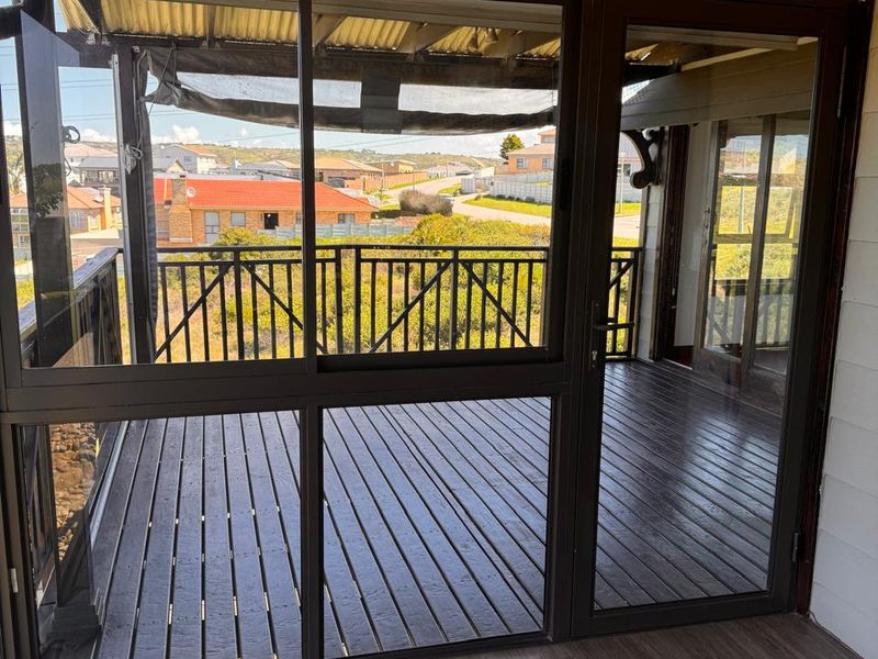 A covered patio area featuring timber decking, sliding glass doors, and a metal balustrade, offering an outdoor space with views of the surrounding neighborhood.