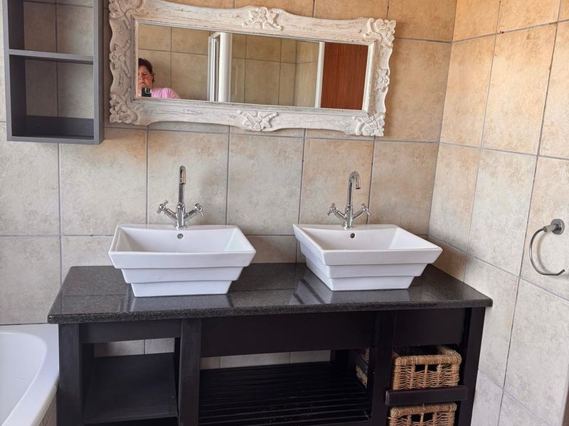 A bathroom featuring a double vanity with granite countertop, dual vessel sinks, chrome faucets, and full-height wall tiling.