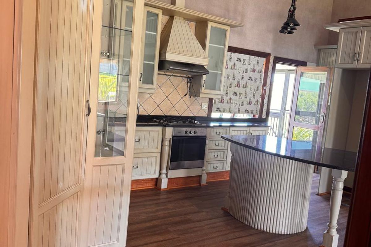 Spacious kitchen featuring vaulted ceilings with exposed timber beams, built-in cabinetry, a gas stove with extractor, and a central island with dark stone countertop.