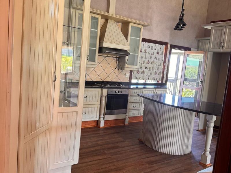 Spacious kitchen featuring vaulted ceilings with exposed timber beams, built-in cabinetry, a gas stove with extractor, and a central island with dark stone countertop.