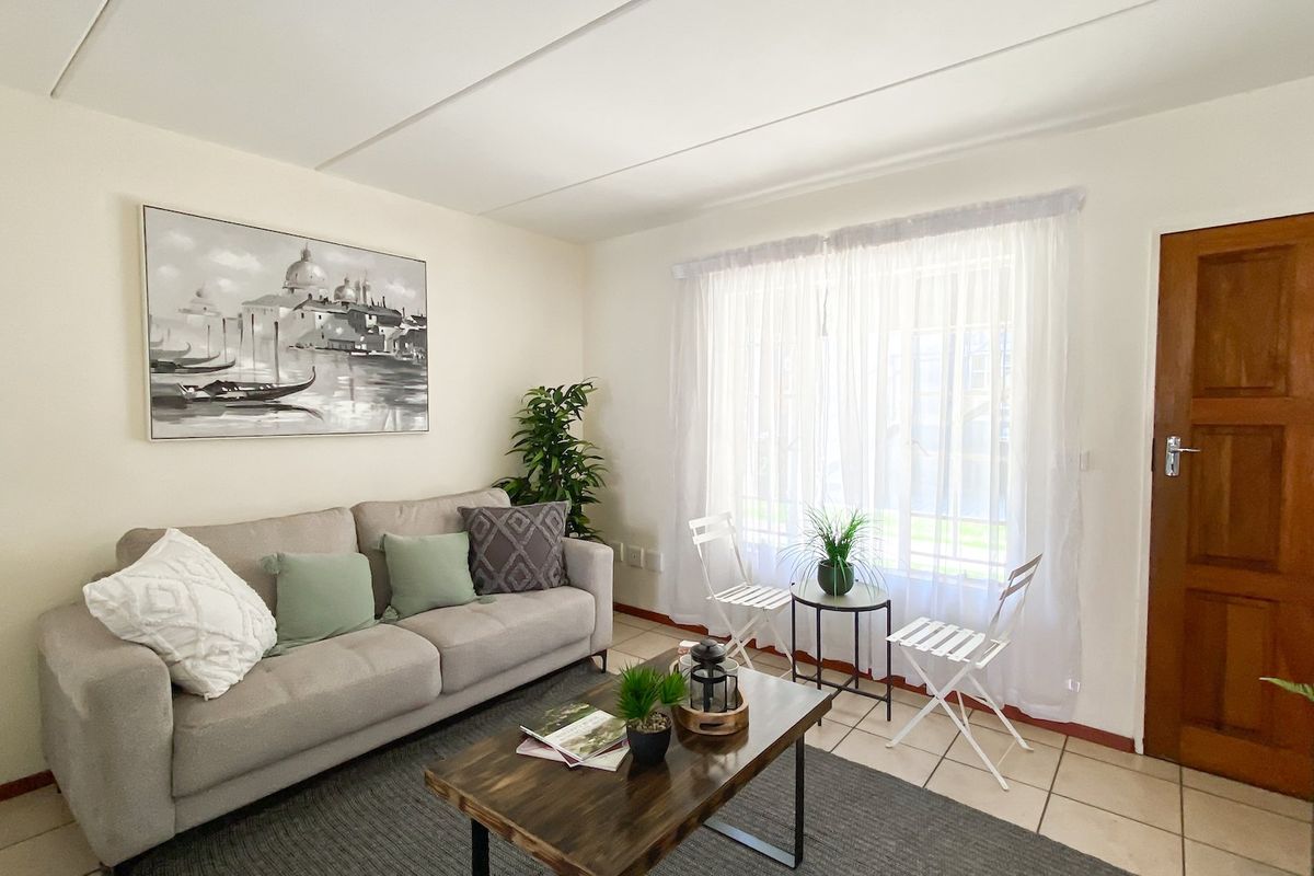 A bright living room featuring neutral tiled flooring, a solid timber door, and large window with natural light.