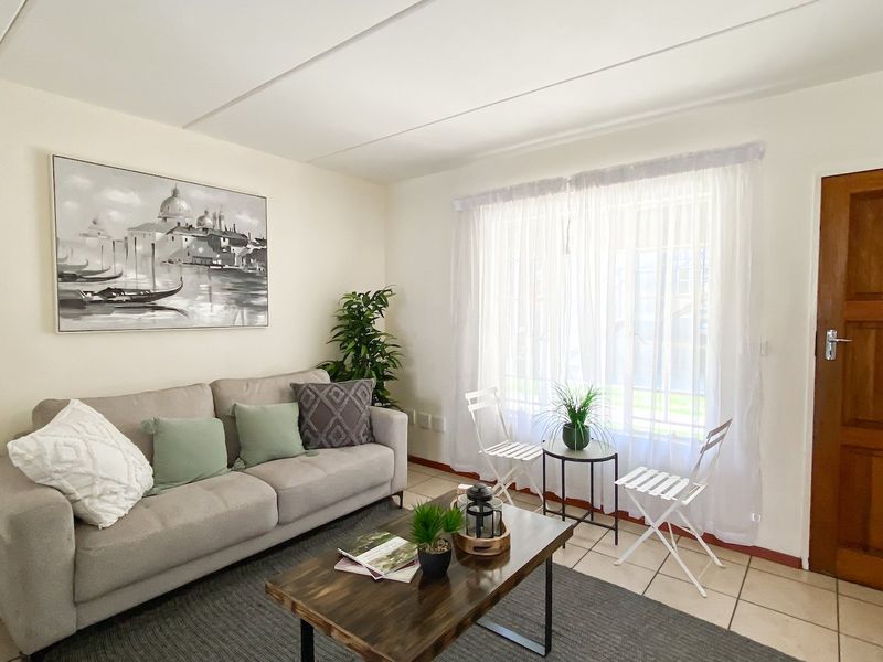 A bright living room featuring neutral tiled flooring, a solid timber door, and large window with natural light.