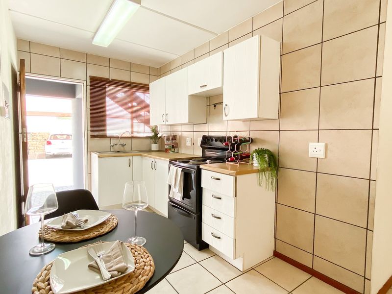 Functional kitchen featuring white cabinetry, tiled backsplash, tiled flooring, and a freestanding stove, with direct access to the exterior.