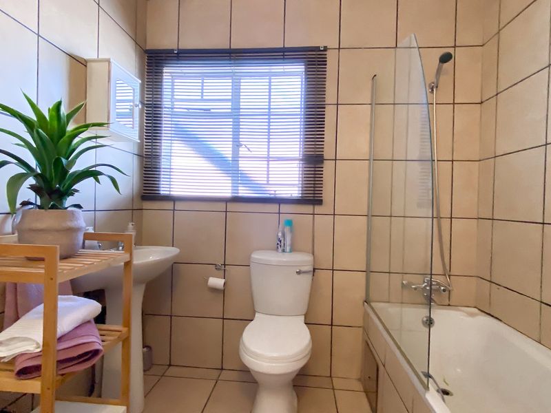 A functional bathroom featuring a pedestal basin, toilet, and a bathtub with a glass shower screen, finished with neutral wall and floor tiles.