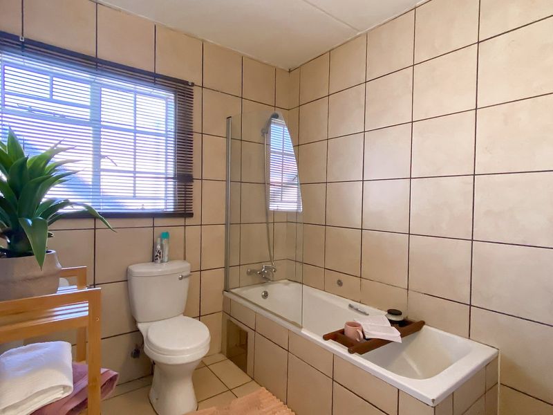 A functional bathroom featuring a bathtub with a glass shower screen, a toilet, and full-height wall tiling.