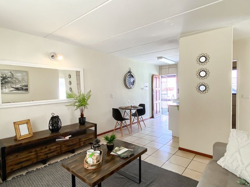 An open-plan living and dining area featuring tiled flooring, neutral walls, and a partition wall leading to the entrance.