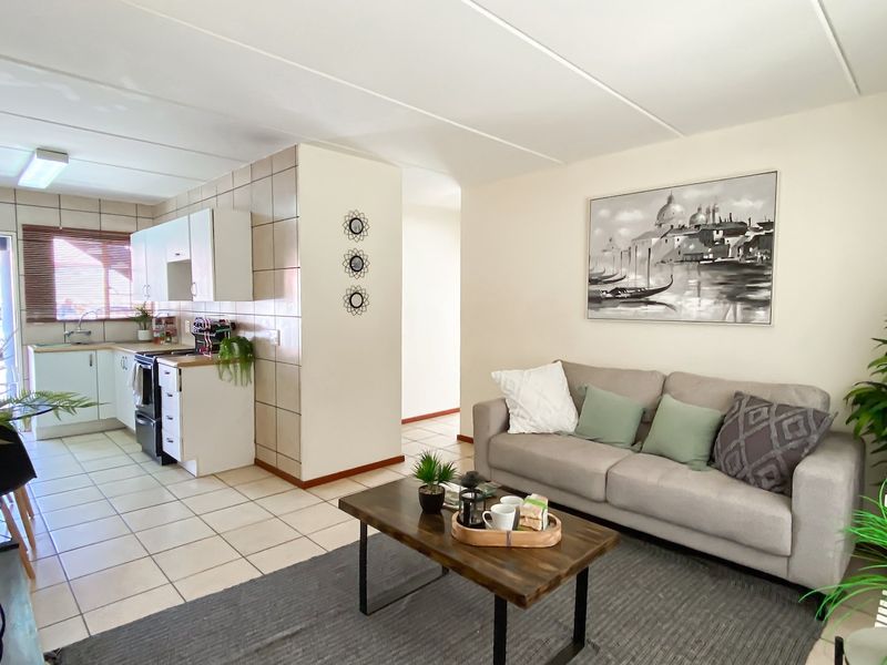 Open-plan living area featuring a functional kitchen with tiled backsplash and cabinetry, seamlessly flowing into a comfortable lounge space with tiled flooring throughout.