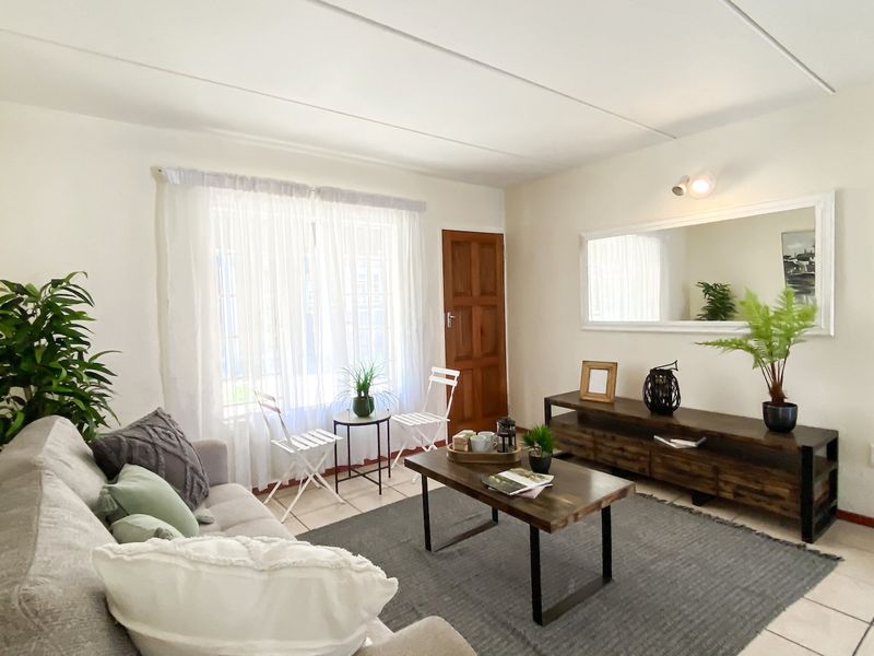 A bright and functional living room featuring tiled flooring, a timber entrance door, and neutral wall finishes, offering a comfortable and inviting living space.