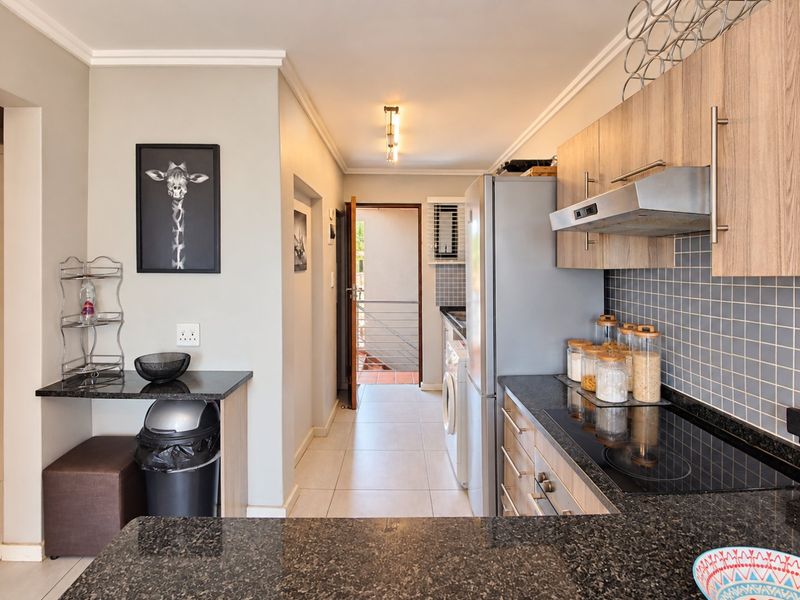 Modern kitchen featuring granite countertops, built-in cabinetry, electric hob with extractor fan, and tiled backsplash, leading to an adjacent utility area.