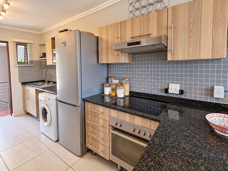 Modern kitchen featuring light wood cabinetry, dark granite countertops, tiled backsplash, and integrated appliances including an oven, hob, and extractor fan.