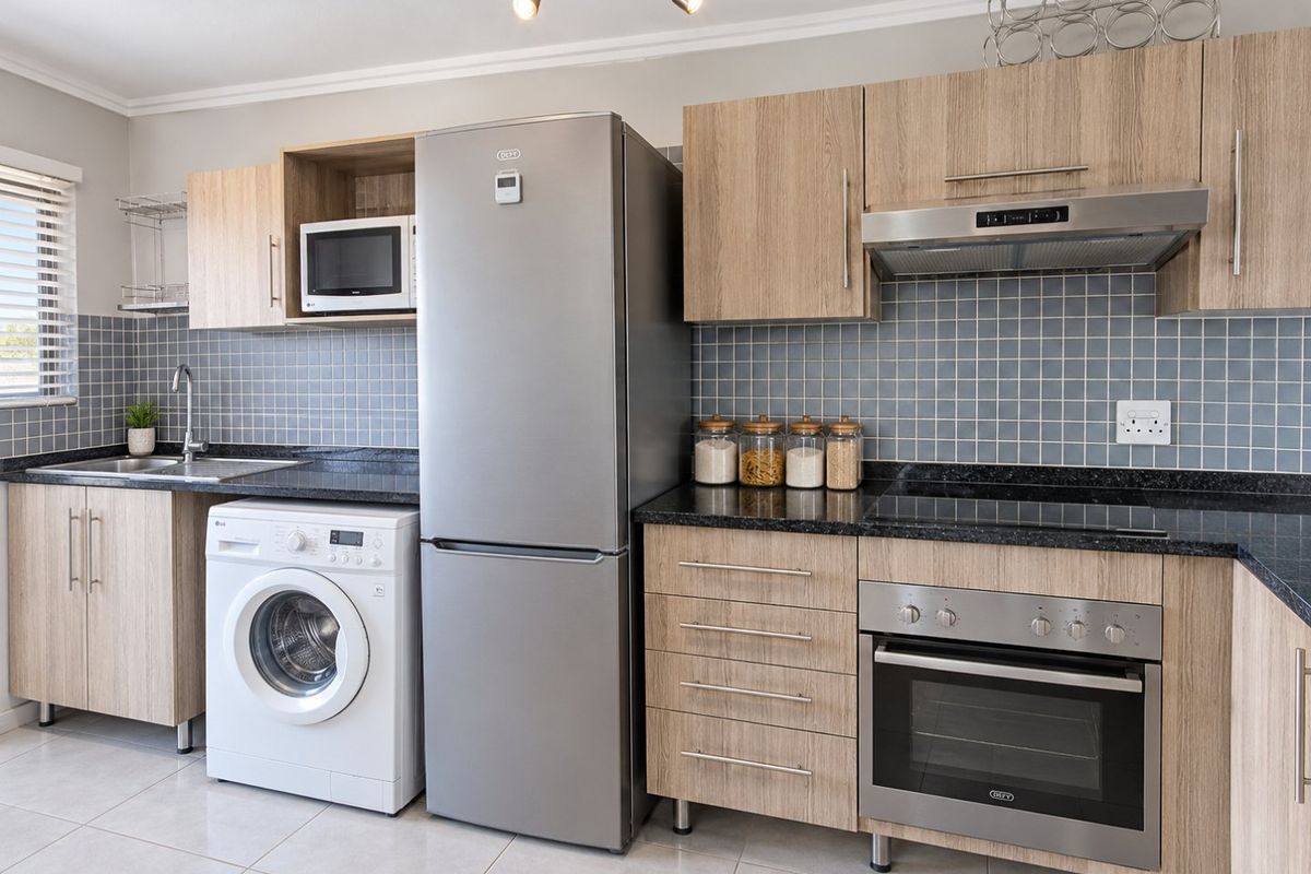 Modern kitchen featuring light wood cabinetry, granite countertops, tiled backsplash, and integrated appliances including an oven, hob, and extractor fan.