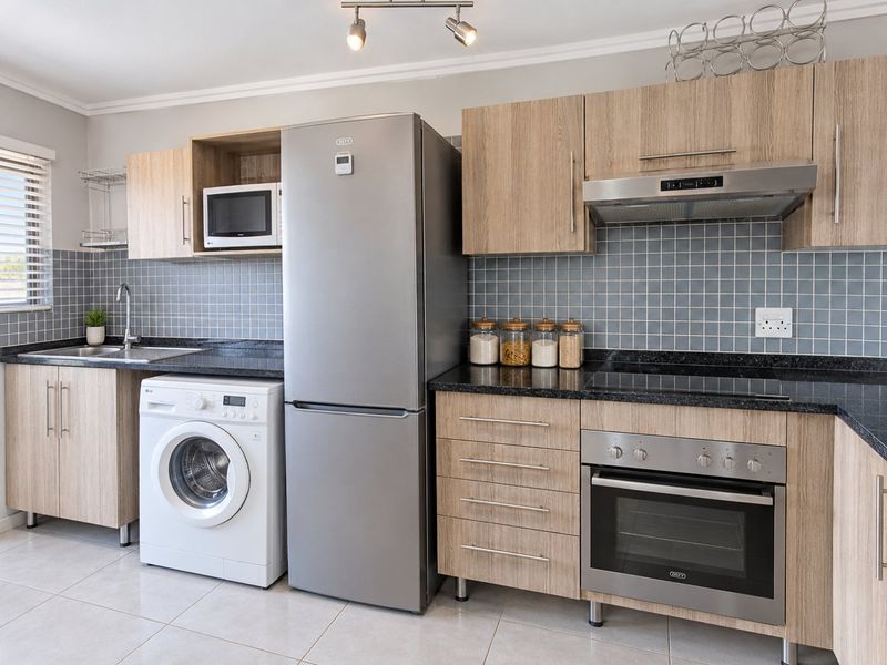 Modern kitchen featuring light wood cabinetry, granite countertops, tiled backsplash, and integrated appliances including an oven, hob, and extractor fan.