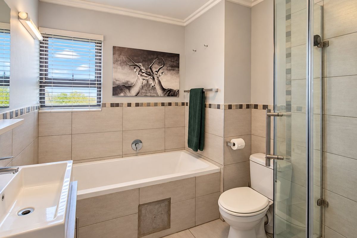 Modern bathroom featuring a built-in bathtub, separate glass shower enclosure, wall-mounted basin, and neutral tiled finishes throughout.