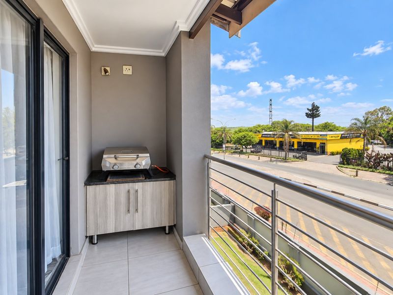 A covered balcony featuring tiled flooring, a built-in cabinet with a stone countertop, and a stainless steel railing overlooking the street.