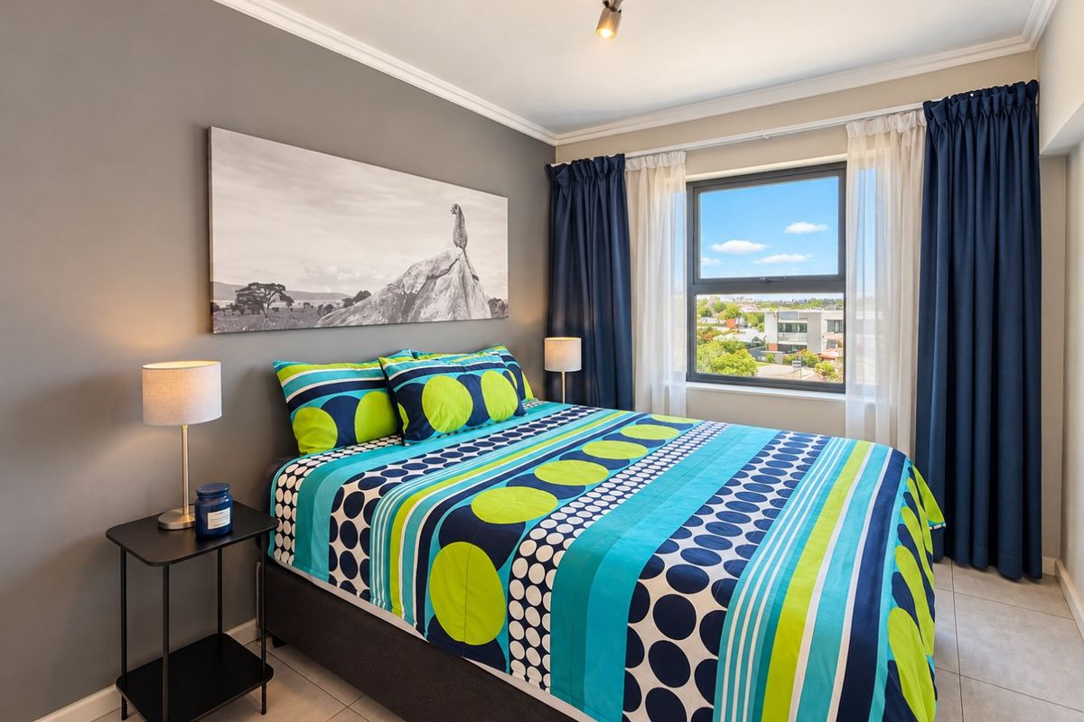 A well-maintained bedroom featuring tiled flooring, modern track lighting, and a window with views, finished with neutral grey walls and decorative ceiling cornicing.