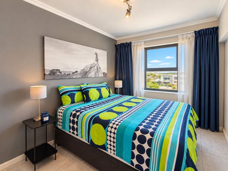 A well-maintained bedroom featuring tiled flooring, modern track lighting, and a window with views, finished with neutral grey walls and decorative ceiling cornicing.