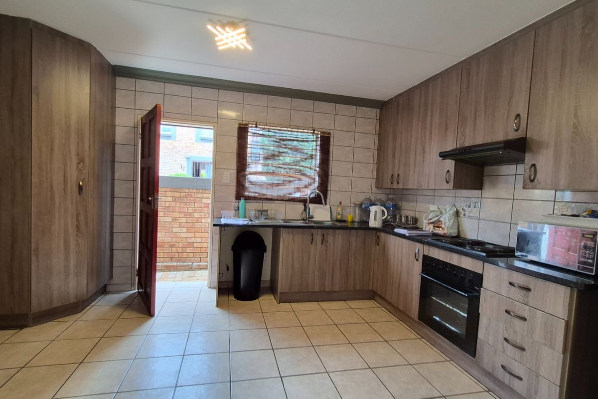 A functional kitchen featuring wood-look cabinetry, built-in oven and hob, tiled flooring, and direct access to an outdoor area.