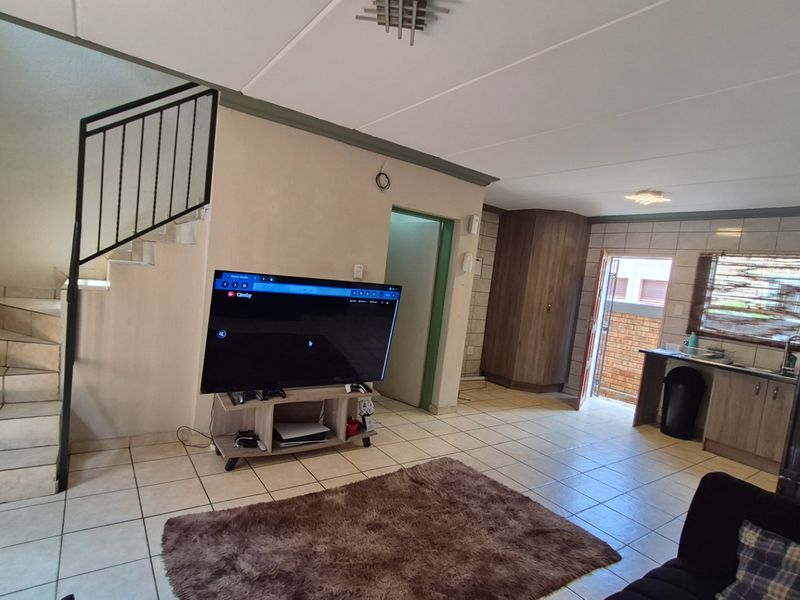Open plan living area featuring tiled flooring, a staircase with metal railing, and a functional kitchen space with built-in cabinetry.