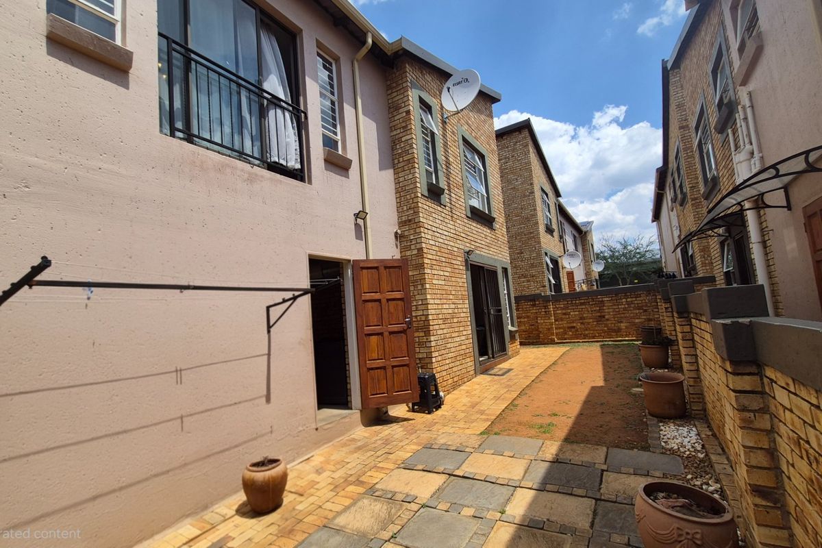A rear exterior view of a townhouse featuring a paved courtyard, brick facade, and wall-mounted clothesline.