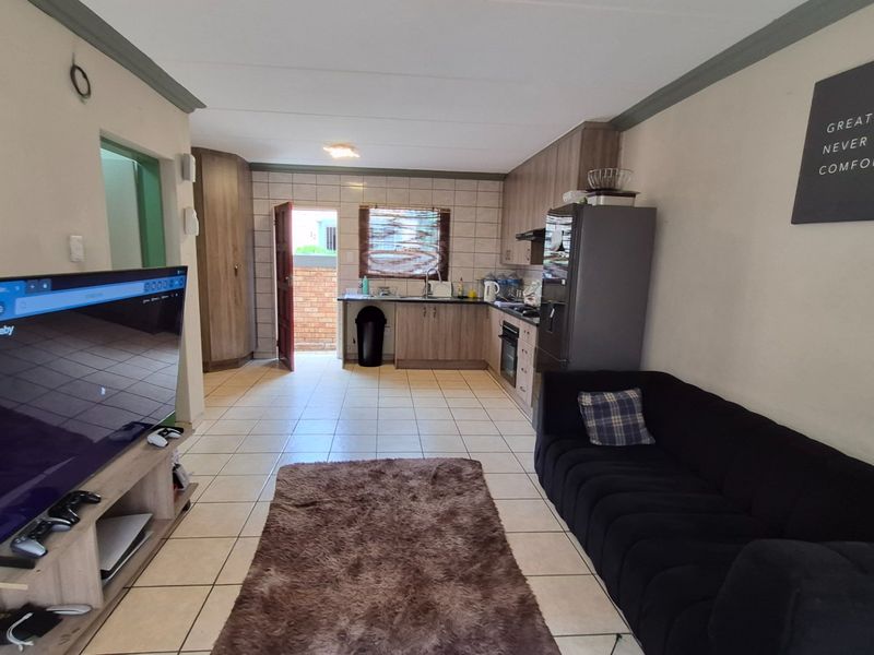 Open-plan living area featuring tiled flooring and a functional kitchen with built-in cabinetry, oven, and hob, leading to an external door.