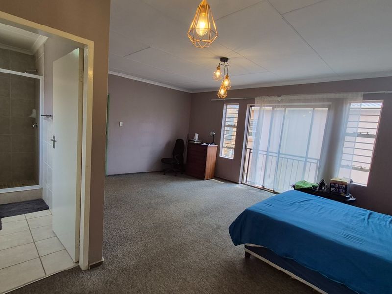 Spacious bedroom featuring an en-suite bathroom, carpeted flooring, and a sliding glass door leading to an outdoor area.