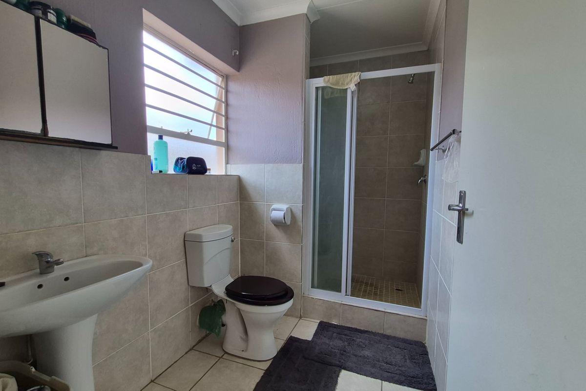 A functional bathroom featuring a pedestal basin, toilet, and a tiled shower enclosure with a louvered window for ventilation.