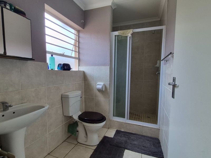 A functional bathroom featuring a pedestal basin, toilet, and a tiled shower enclosure with a louvered window for ventilation.