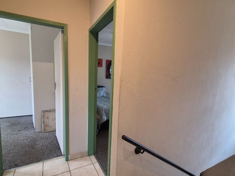 A hallway area featuring tiled flooring, a wall-mounted handrail, and access points to adjacent rooms with painted door frames.