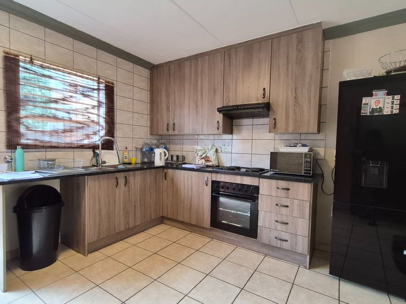 A functional kitchen featuring wood-look laminate cabinetry, built-in oven and hob, tiled backsplash, and tiled flooring with direct access to an outdoor area.