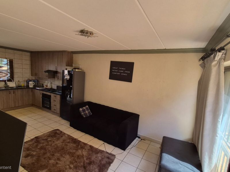 Open-plan living area featuring a functional kitchen with built-in cabinetry and tiled flooring, seamlessly connected to a bright living space with sliding door access.