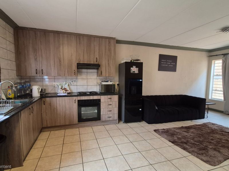 Open-plan kitchen and living area featuring wood-look cabinetry, built-in cooking appliances, tiled flooring, and neutral wall finishes.