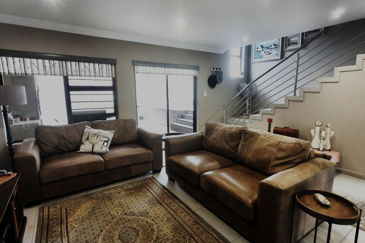 A well-lit living room featuring tiled flooring, a modern staircase with stainless steel balustrades, and sliding glass doors leading to an outdoor area.