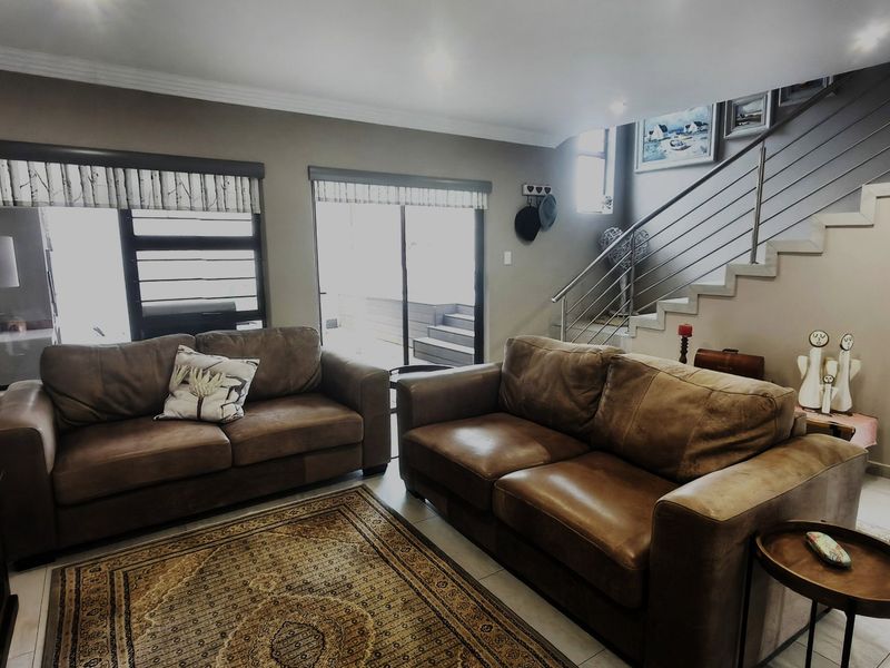 A well-lit living room featuring tiled flooring, a modern staircase with stainless steel balustrades, and sliding glass doors leading to an outdoor area.