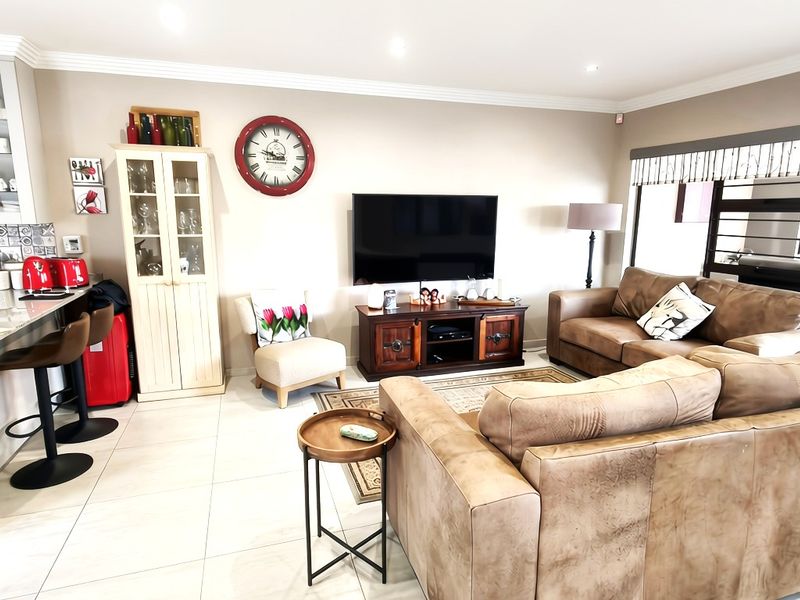 A bright open-plan living and kitchen area featuring tiled flooring, modern cabinetry, granite countertops, and direct access to an outdoor space via sliding doors.