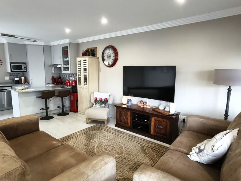 An open-plan living and kitchen area featuring modern cabinetry, stone countertops, integrated appliances, recessed lighting, and tiled flooring throughout.