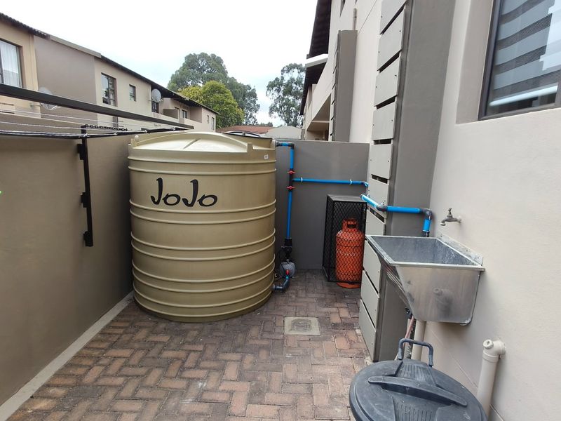 A functional outdoor utility area featuring a water storage tank, a wall-mounted utility sink, and paved flooring, situated along the side of the property.