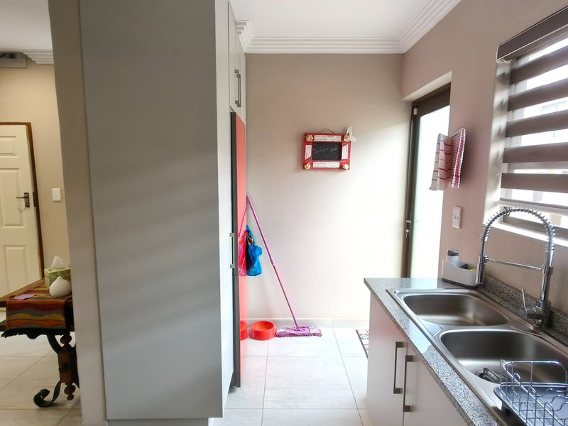 A functional scullery area featuring a double bowl stainless steel sink, granite countertops, and built-in cabinetry, providing additional workspace and storage.