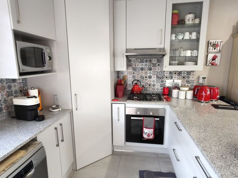 Modern kitchen featuring granite countertops, built-in oven, gas hob, extractor fan, and ample fitted cabinetry with a decorative tiled backsplash.