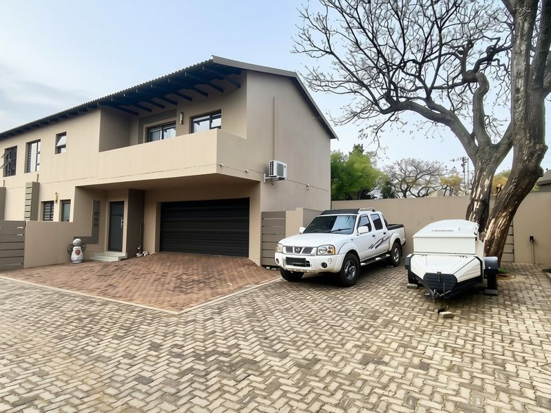 Front elevation of a modern double-story townhouse featuring a paved driveway, double garage, and an upper-level balcony.