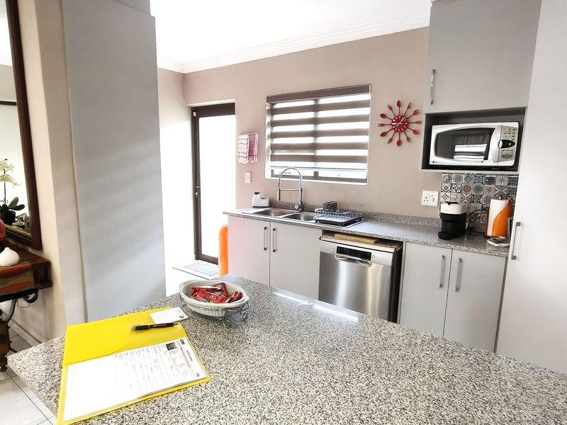 Modern kitchen featuring granite countertops, built-in cabinetry, stainless steel dishwasher, integrated microwave, and a tiled backsplash with convenient access to the exterior.