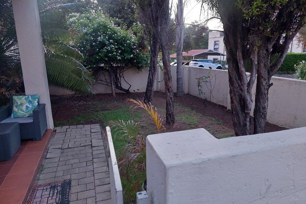 A private rear garden area featuring a paved walkway, tiled patio space, and perimeter boundary walling.