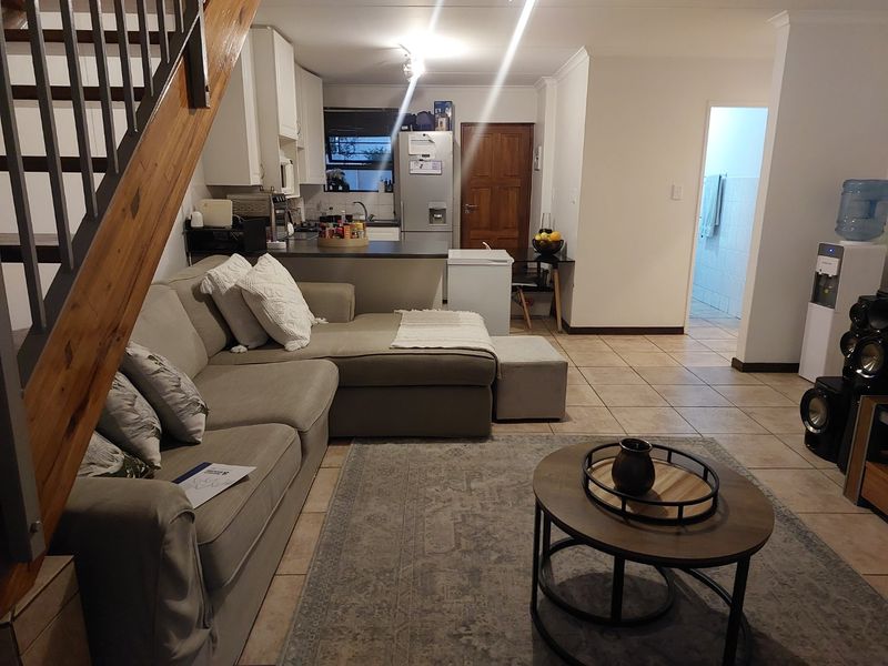 Open plan living area featuring tiled floors, a functional kitchen with cabinetry, and a staircase leading to the upper level.