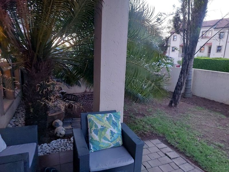 A covered patio area featuring a paved floor and structural column, overlooking a private garden space with boundary walling.