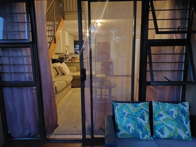 View from a patio through a sliding glass door into an open plan living and kitchen area with an internal staircase.