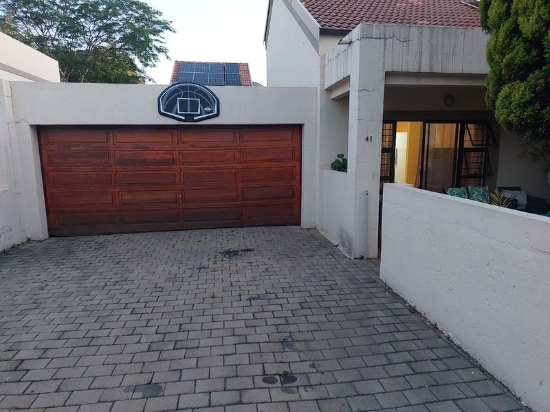 Front exterior view of the apartment featuring a wooden garage door, paved driveway, and a small covered entrance area.