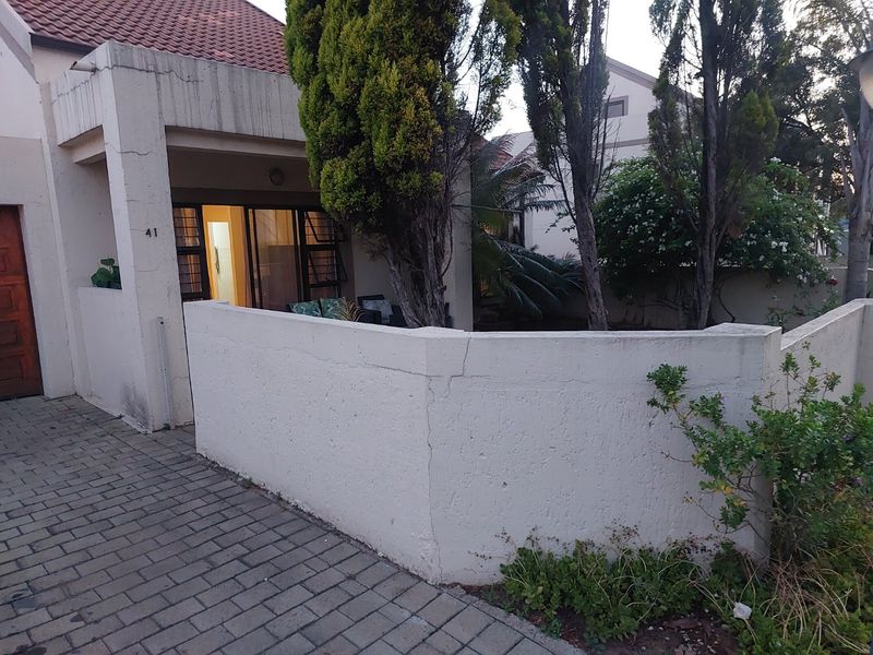 Front exterior view of the apartment featuring a paved driveway, a private entrance with a security gate, and a surrounding boundary wall.