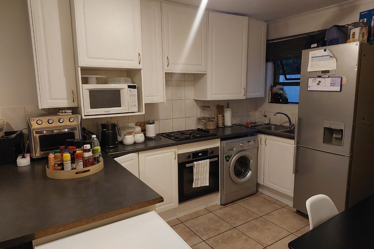 A functional kitchen featuring white cabinetry, dark countertops, tiled backsplash, and integrated appliances including an oven, hob, and washing machine.